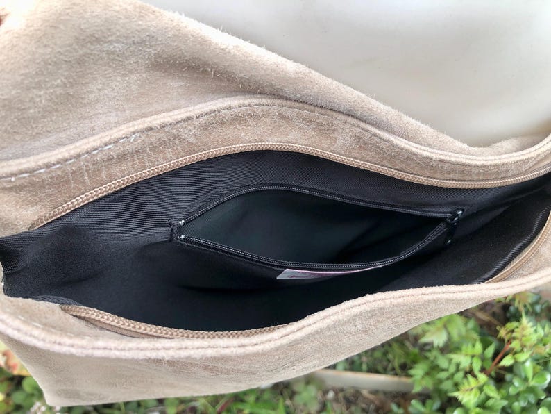 May include: A beige suede bag with a black zippered pocket inside. The bag is open and the inside is visible.