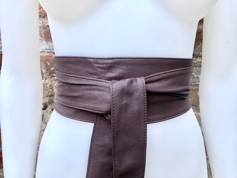 Op de afbeelding: Een bruine leren riem om een ​​taille geknoopt. De riem is breed en heeft een eenvoudig ontwerp.
