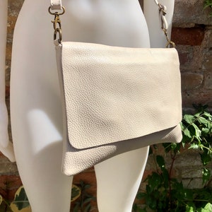 May include: A light beige leather crossbody bag with a flap closure and a gold-toned chain strap.