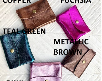 May include: Five small, square coin purses in metallic shades of copper, fuchsia, teal green, metallic brown, and pink. Each purse features a snap closure. The purses are arranged on a white surface, with each colour labelled in bold text.
