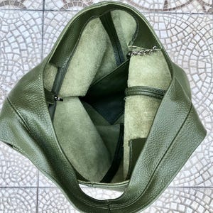 May include: An overhead view of a green leather tote bag. The bag is open, revealing a lighter green interior with a zippered pocket and a small chain. The leather has a textured appearance.