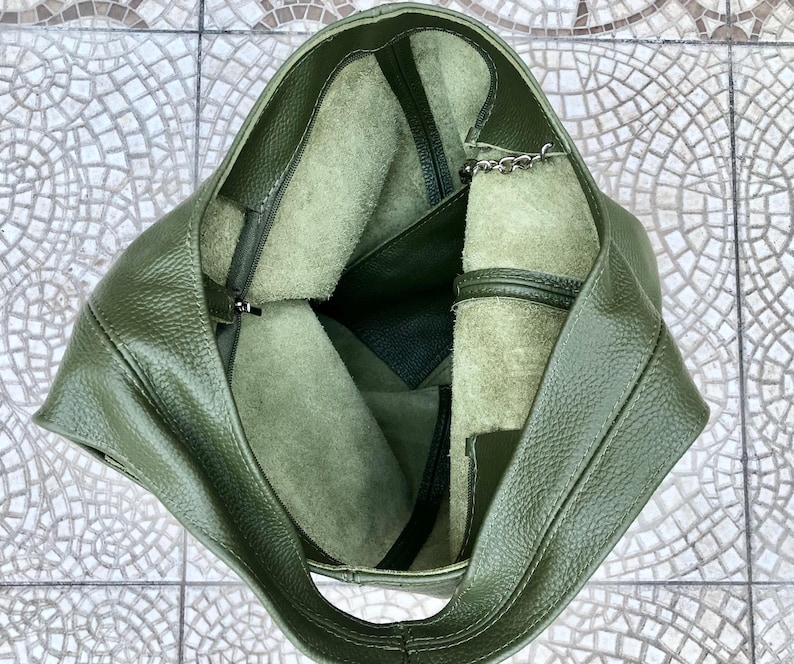 May include: An overhead view of a green leather tote bag. The bag is open, revealing a lighter green interior with a zippered pocket and a small chain. The leather has a textured appearance.