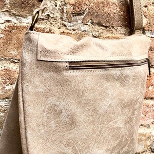 May include: A beige leather crossbody bag with a zippered pocket and a brown strap.