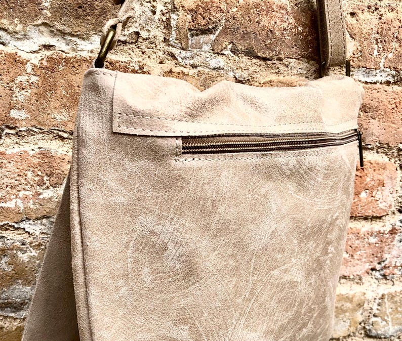 May include: A beige leather crossbody bag with a zippered pocket and a brown strap.