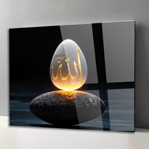 May include: A glowing, egg-shaped object featuring gold Arabic calligraphy, balanced atop a dark, textured, oval-shaped stone. The composition is set against a dark, reflective background with a subtle cross-shaped shadow pattern.