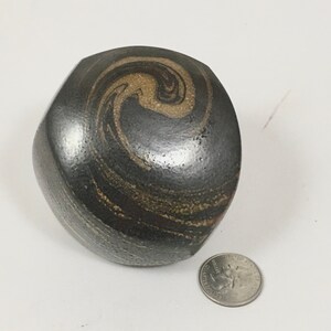 May include: A black ceramic vase with a swirling brown and gold pattern. The vase is round and has a slightly uneven surface.