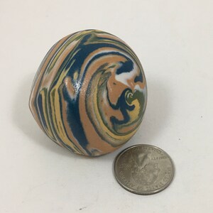May include: A small, round, ceramic ornament with a swirling pattern of blue, yellow, white, and brown.