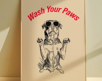 Puede incluir: Un estampado enmarcado con una ilustración en blanco y negro de un perro con gafas de sol y levantando las patas. Las palabras "Wash Your Paws" están arqueadas sobre el perro en rojo. La obra de arte está sobre un fondo beige.
