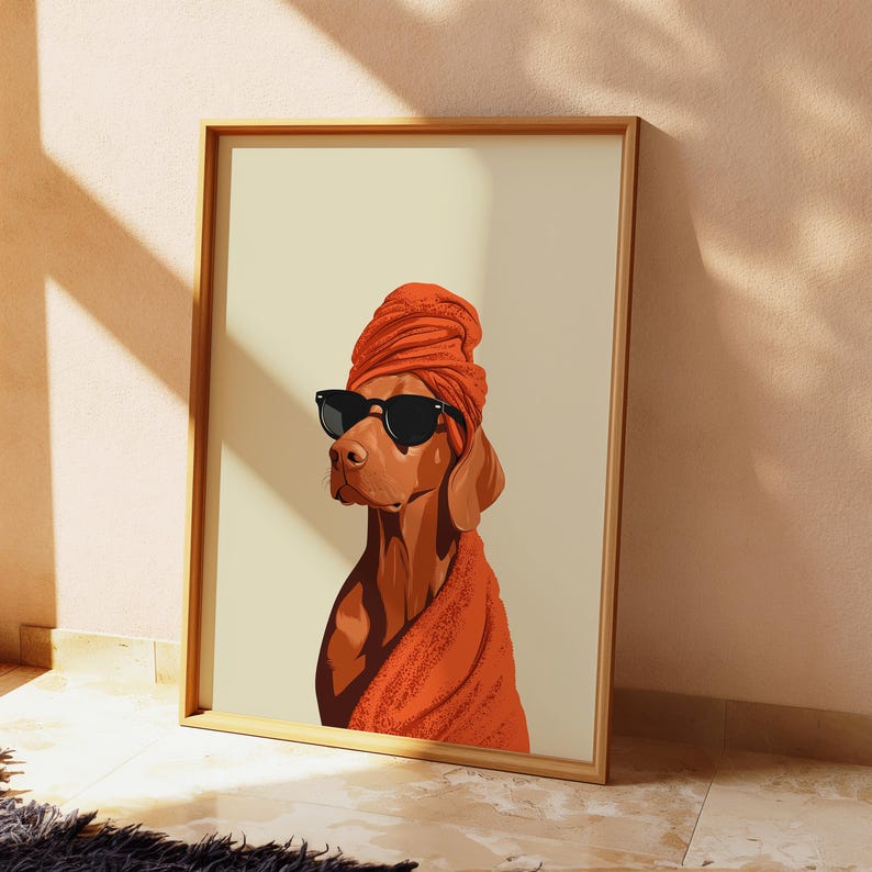May include: A framed art print depicting a brown dog wearing black sunglasses and an orange head wrap and shawl. The dog is set against a cream-coloured background. The artwork is in a wooden frame.