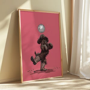 May include: A framed print showing a brown dog in cowboy boots, playing with a disco ball. The dog is standing upright against a pink backdrop. The artwork is presented in a wooden frame.