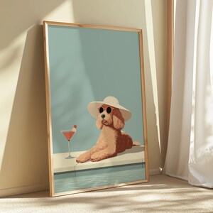 Puede incluir: Una impresión artística enmarcada representa un caniche con gafas de sol y un sombrero para el sol, descansando junto a una piscina con un cóctel. El perro es marrón claro, el sombrero es blanco y la bebida es roja.