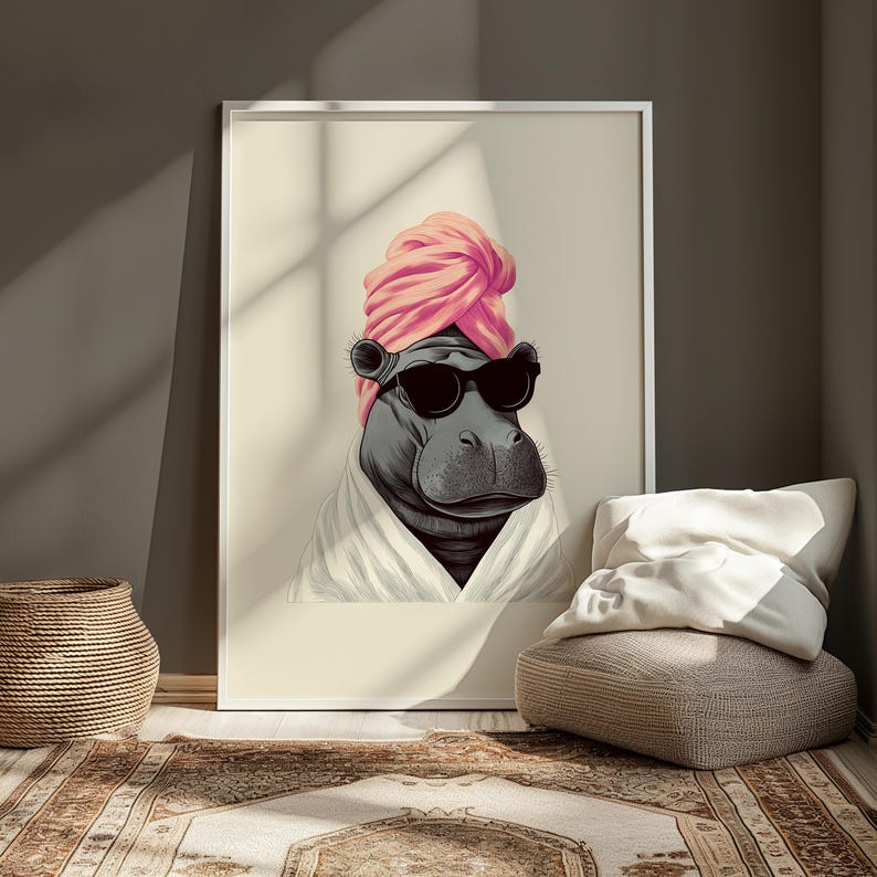 May include: A framed art print featuring a hippopotamus wearing sunglasses, a pink turban, and a white robe. The artwork is displayed in a room with a woven basket, a patterned rug, and a beige ottoman with pillows.