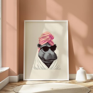 May include: A framed art print featuring a hippo wearing sunglasses and a pink turban, wrapped in a white robe. The hippo's portrait is set against a neutral background, creating a whimsical and stylish aesthetic.