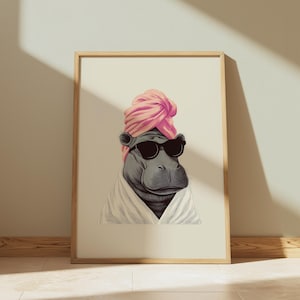 May include: A framed print featuring a hippopotamus wearing sunglasses, a pink turban, and a white robe. The artwork has a whimsical, spa-day theme, with the hippo's relaxed expression and attire. The image is set against a neutral background.