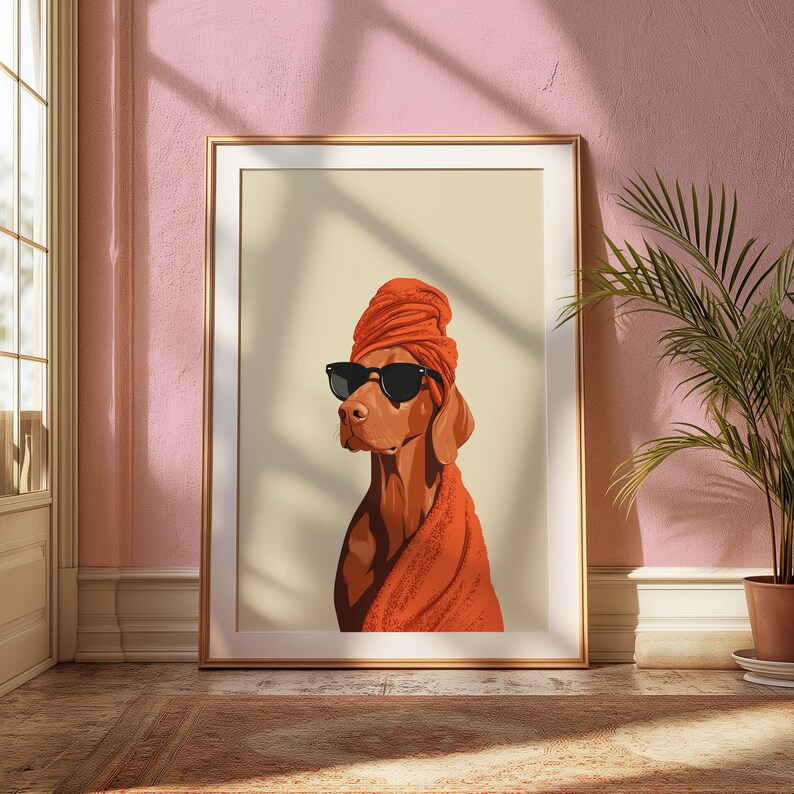 May include: A framed art print depicting a dog in black sunglasses, an orange head wrap, and a matching towel. The dog is a reddish-brown colour. The artwork is presented in a gold frame against a cream background, creating a stylish aesthetic.