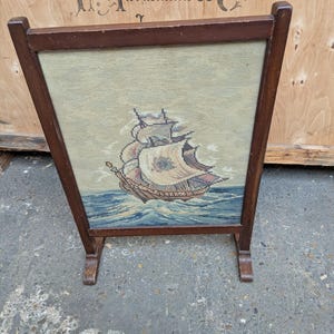 Peut inclure: Un écran de cheminée vintage en bois avec un motif de tapisserie représentant un voilier sur une mer bleue agitée. Le cadre en bois est de couleur marron foncé. La tapisserie a un fond vert clair. Mesure environ 60 cm de haut.
