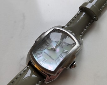 Puede incluir: Un reloj Invicta plateado con esfera nacarada y números romanos. El reloj tiene una caja rectangular y una correa de cuero verde oliva brillante. Las palabras "Special Edition" son visibles en la esfera.