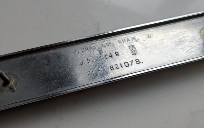 May include: A rectangular, silver-colored metal plate with engraved text. The text includes "J. FRAY LTD. BHAM", "J.F. 4149.", and "P.N. 621078.". The plate has a slightly worn appearance, suggesting age or use. A small, circular attachment is visible on the left side.