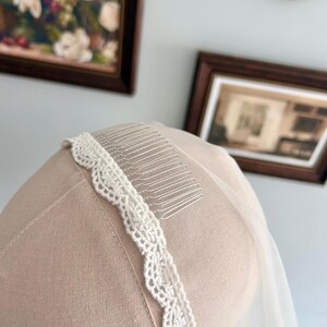 May include: A bridal veil with a delicate, scalloped lace trim and a comb for secure placement in the hair. The veil is a soft white color, and the lace trim adds a touch of elegance. The comb is silver.