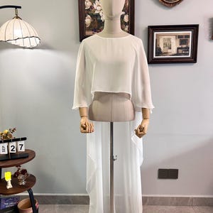 Puede incluir: Un conjunto blanco y fluido de dos piezas exhibido en un maniqu&iacute;. La parte superior es un dise&ntilde;o corto de manga corta, y la parte inferior es una falda larga y transparente. El conjunto est&aacute; hecho de una tela ligera, ideal para una ocasi&oacute;n especial.