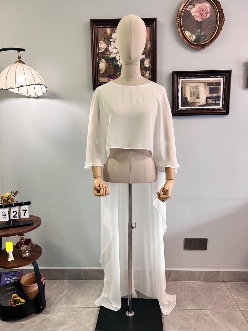 Puede incluir: Un conjunto blanco y fluido de dos piezas exhibido en un maniqu&iacute;. La parte superior es un dise&ntilde;o corto de manga corta, y la parte inferior es una falda larga y transparente. El conjunto est&aacute; hecho de una tela ligera, ideal para una ocasi&oacute;n especial.