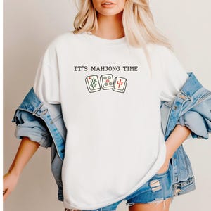 A woman wearing a white t-shirt with the text "IT'S MAJONG TIME" printed on it, along with a graphic of a game of mahjong tiles.