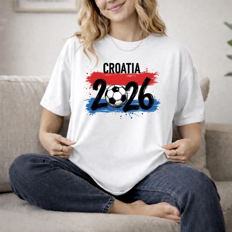 May include: White t-shirt with a graphic design featuring the word "CROATIA" above the numbers "2026" and a soccer ball. The design incorporates red, white, and blue colors, resembling a flag.