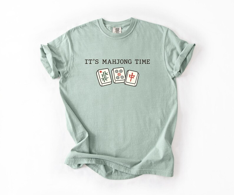 A light green t-shirt with the text "IT'S MAHJONG TIME" printed on it, along with illustrations of playing cards.