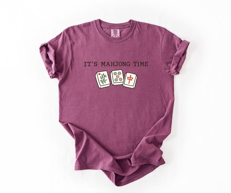 A purple t-shirt with the text "IT'S MAJONG TIME" printed on it, along with a graphic of a mahjong tile.
