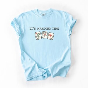 A light blue t-shirt with the text "IT'S MAHJONG TIME" printed on it, along with a graphic of a mahjong tile.