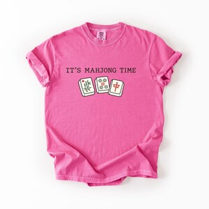A pink t-shirt with the text "IT'S MAJONG TIME" printed on it, along with a graphic of a mahjong tile.