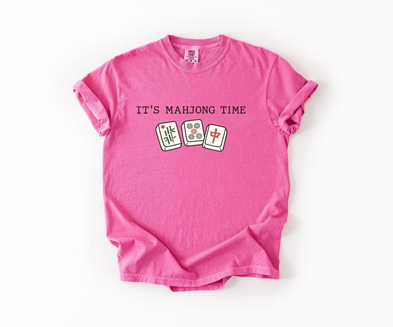 A pink t-shirt with the text "IT'S MAJONG TIME" printed on it, along with a graphic of a mahjong tile.