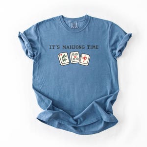 A blue t-shirt with the text "IT'S MAJONG TIME" printed on it, along with a graphic of a mahjong tile.