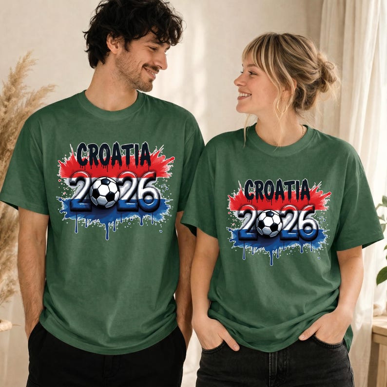 May include: Two people wearing matching green t-shirts. The shirts feature the word "CROATIA" above the number "2026" with a soccer ball in the center. The design incorporates red, white, and blue colors, resembling a flag.
