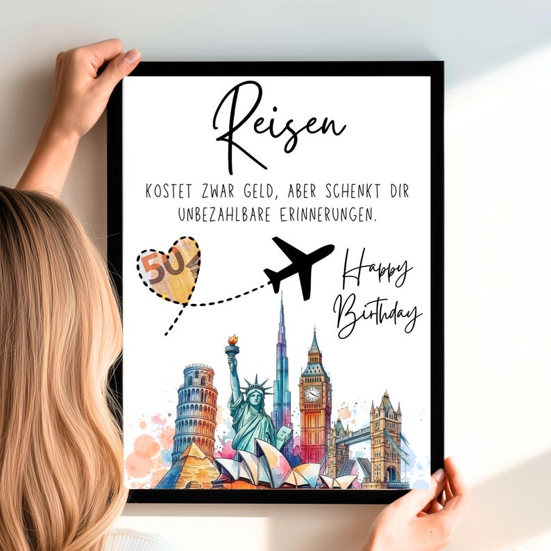 May include: A framed print with the German word "Reisen" at the top, meaning "travel". The print features a black airplane, a heart with "50" inside, and famous landmarks. The text "Happy Birthday" is also included.
