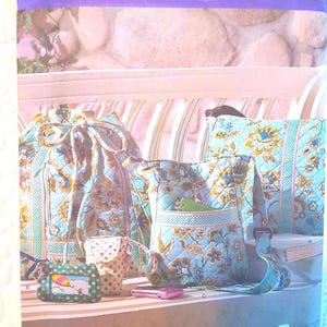May include: A Simplicity sewing pattern envelope 2911 featuring a collection of quilted bags in a light blue fabric with a yellow and brown floral pattern. The set includes a drawstring bag, a crossbody bag, a small pouch, and a card holder.