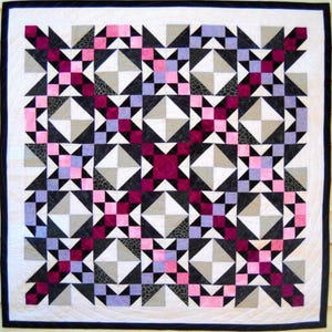 Peut inclure: Une courtepointe carrée avec une bordure blanche et une reliure noire. La courtepointe présente un motif géométrique répétitif de carrés, de triangles et d'éclats d'étoiles dans des tons de rose, de violet, de gris et de noir. La courtepointe est probablement faite à la main.