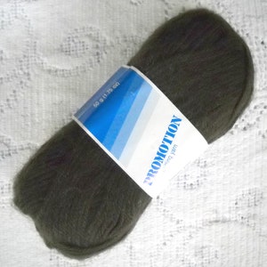 May include: A dark olive green ball of knitting yarn with a white and blue label. The label reads "PROMOTION knitting yarn" and "50 g (1.75 oz)". The yarn is tightly wound and appears soft. The background is a white, patterned fabric.