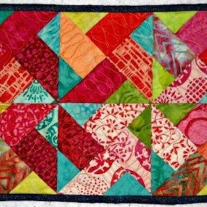May include: A rectangular, colorful quilt with a dark blue border. The quilt features a geometric pattern of triangles and diamonds in various shades of red, pink, orange, green, and blue. The fabric has a variety of patterns.