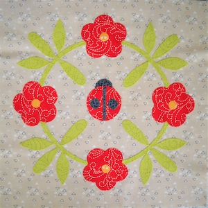 May include: A square fabric block featuring a floral design with red flowers, green leaves, and a ladybug in the center. The flowers and ladybug are appliqued with white stitching. The background is a light tan color with small white triangles.