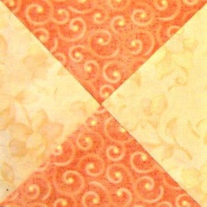 Op de afbeelding: Een quiltblok met vier vierkanten, twee zijn oranje met een wit swirl-patroon en twee zijn geel met een wit bloemenpatroon.