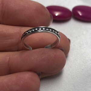 May include: A silver-toned metal ring featuring a continuous row of small, raised spherical beads along the center of the band. The ring has an open design with a small gap at the bottom, allowing for slight adjustments to the fit of the band.