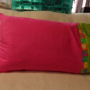 Puede incluir: Una almohada rosa con un borde estampado de flores verdes y amarillas.