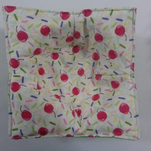 May include: A white fabric bowl liner with a cherry and sprinkle pattern. The liner is quilted and has a green border.