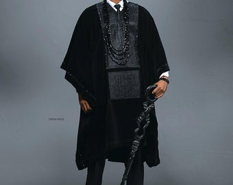 Può includere: Una persona indossa un abito tradizionale nero, composto da cappello, tunica e pantaloni. L'abito presenta ricami e perline intricati. La persona tiene in mano un bastone nero decorativo. Lo sfondo è grigio.