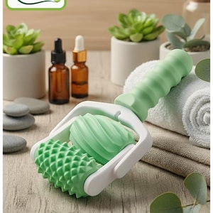 May include: A green and white double roller massage tool. The roller is made of non-toxic bio materials. The handle is green and ribbed, and the rollers have textured surfaces. The text "Rodillo Doble" is visible.