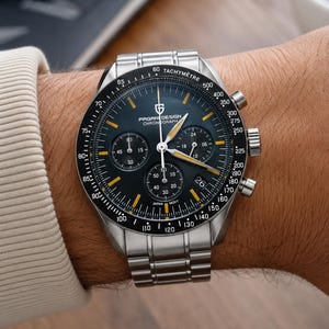 May include: A stainless steel PAGANI DESIGN chronograph watch with a black dial and yellow accents. The watch features multiple sub-dials, a tachymeter bezel, and a stainless steel band. The watch is on a wrist.