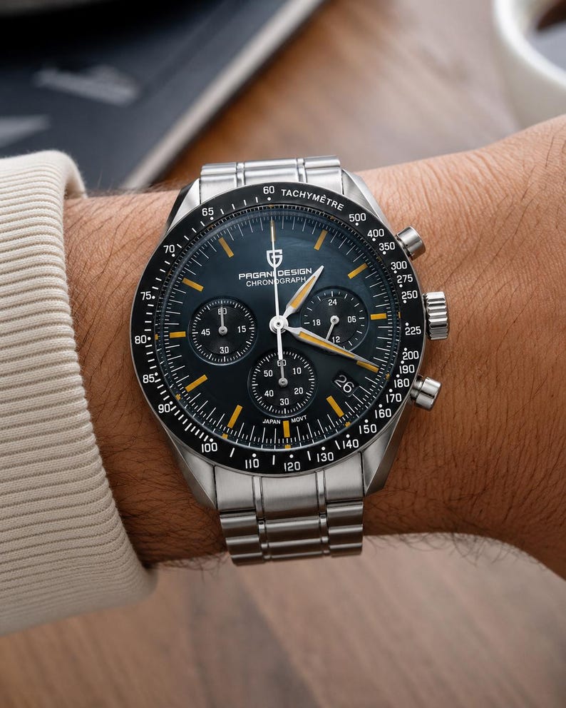 May include: A stainless steel PAGANI DESIGN chronograph watch with a black dial and yellow accents. The watch features multiple sub-dials, a tachymeter bezel, and a stainless steel band. The watch is on a wrist.