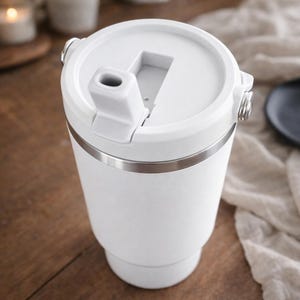 Peut inclure: Un mug de voyage blanc avec une bande en acier inoxydable et un couvercle rabattable. Le mug a une surface texturée et une forme cylindrique, adapté aux boissons chaudes ou froides. Le couvercle comporte un bec verseur et une fermeture sécurisée.