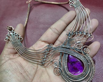 May include: Copper wire necklace featuring a teardrop-shaped, deep purple stone. The pendant is intricately woven with copper wire, showcasing a unique, handcrafted design. The necklace has a delicate chain and a decorative, artistic style.